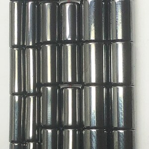 May include: Close-up of a strand of dark gray, cylindrical beads. The beads are arranged in neat rows, reflecting light and appearing smooth. The beads are likely for jewelry making.