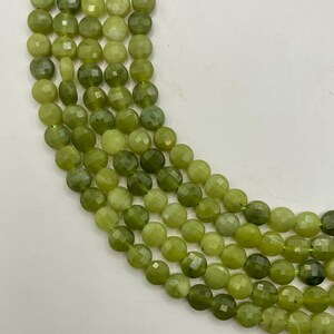 May include: Close-up of several strands of faceted, round, green gemstone beads. The beads vary in shades of green, from light to dark, and are strung together. The background is plain white.