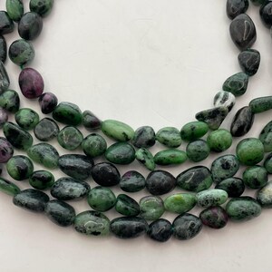May include: Strands of tumbled zoisite beads with ruby inclusions. The beads are a mix of dark green, black, and some with a deep red-purple hue. The beads are strung together, creating a natural and earthy aesthetic.