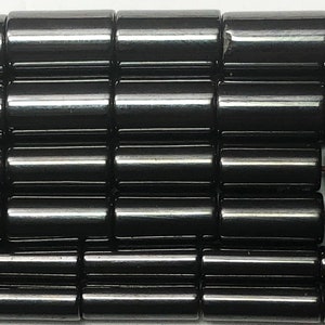 May include: Close-up of a collection of glossy, black cylindrical beads. The beads are arranged in neat rows, reflecting light and creating a smooth, polished appearance. The beads are likely for jewelry making.