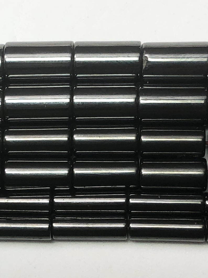 May include: Close-up of a collection of glossy, black cylindrical beads. The beads are arranged in neat rows, reflecting light and creating a smooth, polished appearance. The beads are likely for jewelry making.