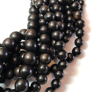 May include: Close-up of strands of dark brown wooden beads. The beads are round and have a smooth, polished finish. The beads are strung together, creating a necklace or bracelet.