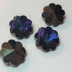 以下が含まれることがあります： 4つの虹色の花型のボタン。各ボタンは、暗いメタリックグレーの縁と、紫、青、緑の色合いを反射する多色のファセットセンターを備えています。ボタンは白い表面に配置されています。