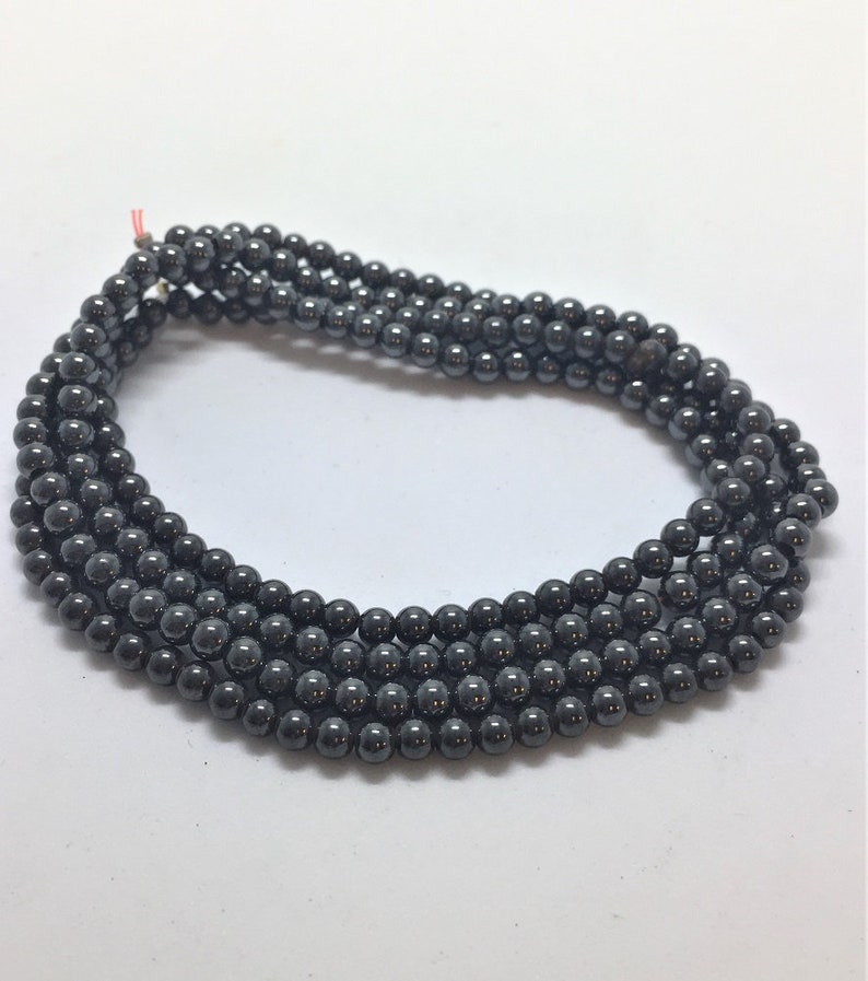 May include: Multiple strands of dark grey hematite beads. The small, round beads are strung together, creating several rows. The beads have a metallic sheen and are displayed against a white background.