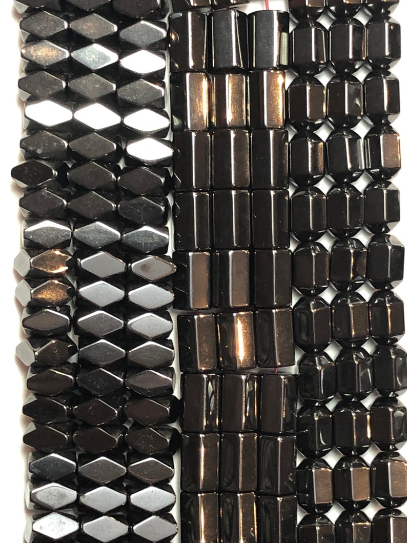 May include: Close-up of three strands of dark gray hematite beads. The beads are in various shapes: diamond, rectangular, and faceted. The beads are strung together, ready for jewelry making. The beads have a polished, reflective surface.