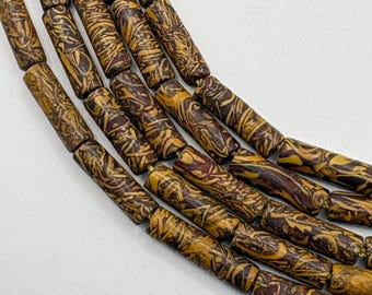 Peut inclure: Gros plan sur plusieurs brins de perles cylindriques. Les perles sont un mélange de marron et de jaune avec un motif tourbillonnant unique. Les perles sont enfilées ensemble, créant un design texturé et visuellement intéressant. Les perles sont probablement utilisées pour la fabrication de bijoux.