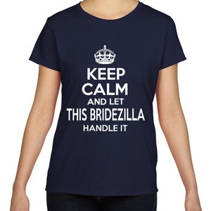 Puede incluir: Una camiseta azul marino de manga corta con un estampado gráfico blanco de una corona sobre el texto "KEEP CALM AND LET THIS BRIDEZILLA HANDLE IT" centrado en el pecho. La prenda tiene un cuello redondo y un corte recto estándar.