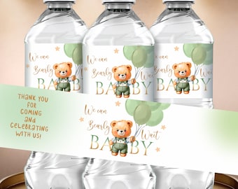 Op de afbeelding: Drie doorzichtige waterflessen met etiketten met een teddybeer met ballonnen. Op de etiketten staat "We can Bearly Wait BABY" in goud en groen. Een banner hieronder zegt "Bedankt voor uw komst en het vieren met ons!"