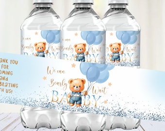 May include: Three clear plastic water bottles with blue and gold labels. The labels feature a cartoon bear holding blue balloons and the text "We can barely wait baby".