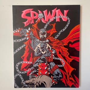 May include: A painting of the comic book character Spawn against a black background. The word "SPAWN" is in red, with a skull above the "A". Spawn is depicted in a dynamic pose, with red cape and chains.