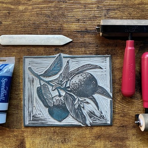 The linoleum block, ink, and rollers used to make this print. The block is a reverse image of the print.