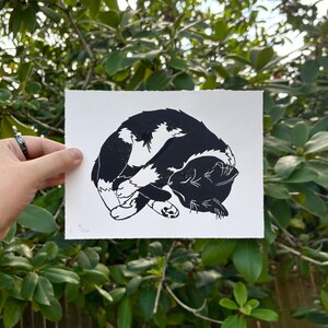 The same cat print in its entirety, viewed straight on held in front of a green rhododendron bush.
