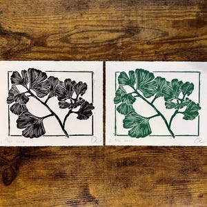 the black ginkgo print is laying on a wooden desk next to a green version of the same print
