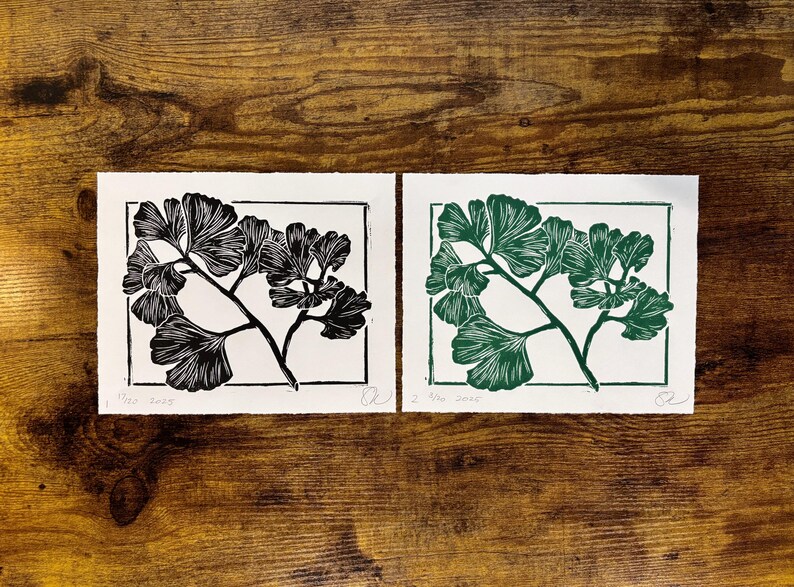the black ginkgo print is laying on a wooden desk next to a green version of the same print