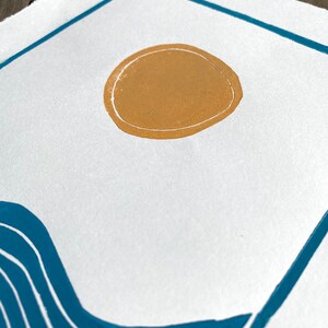 Closeup on the yellow orange sun. it has a white line around the edge and is not quite a perfect circle. The edges of the paper are torn rather than cut, giving a rustic artful look.