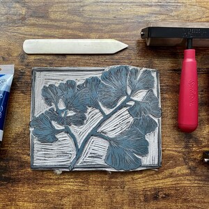 The linoleum block, ink, and rollers used to make this print. The block is a reverse image of the print.