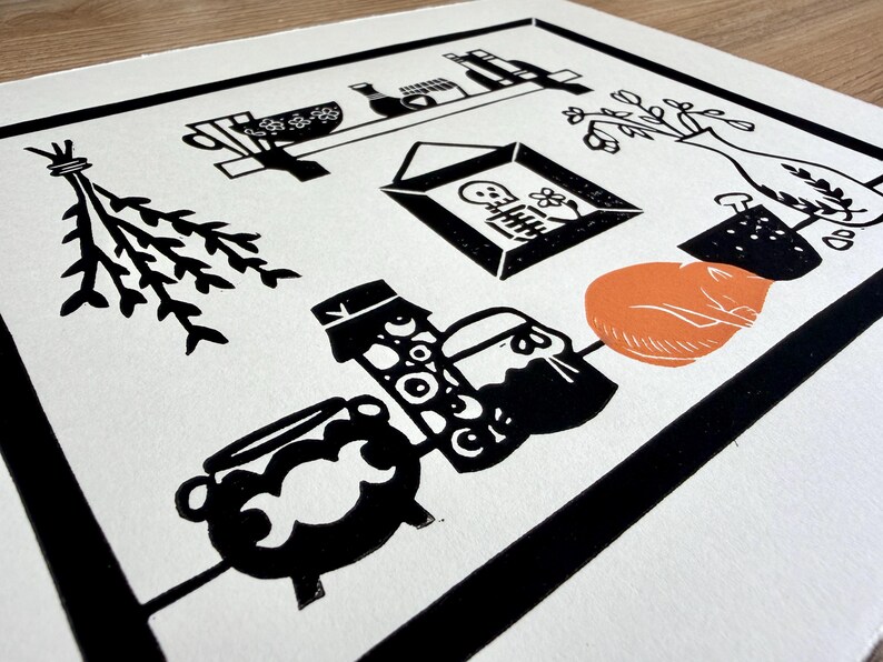 a close-up of the left side of the print. a bundle of herbs is hanging upside down on the wall next to the shelf. there are two jars next to the cat, one of which is full of eyeballs, and a small cauldron with a moon phases design on it.