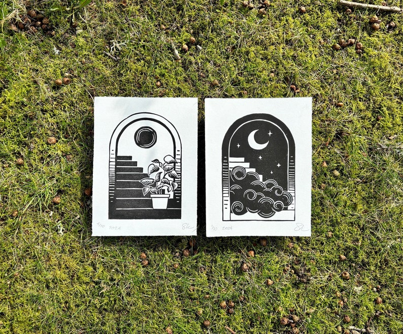 Two black and white prints of arched doorways. The left prints arch has black staircase and sun on white sky and leafy potted plant on bottom stair. The right prints arch has white staircase and moon on black sky. A cloud hides part of the staircase.