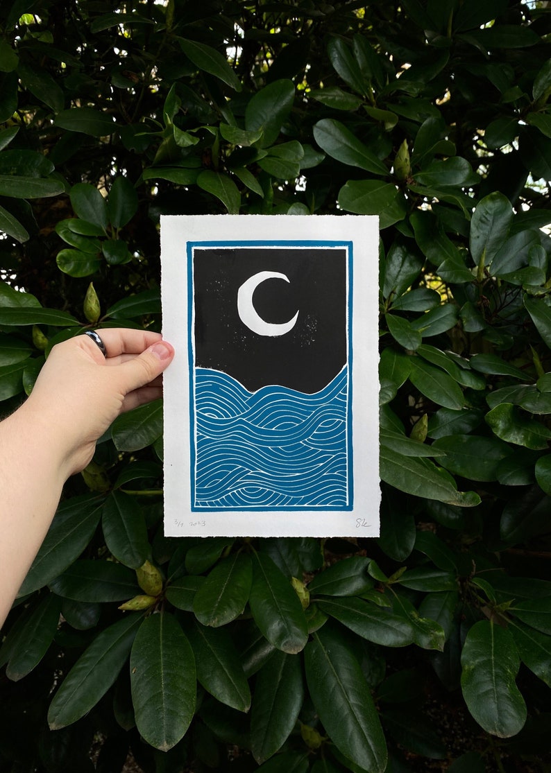 dark blue and black linocut print showing a black night sky with white moon over rolling blue ocean waves. the print is seven inches wide and ten inches tall and has a blue border. the waves have curved lines reminiscent of Japanese woodblock prints