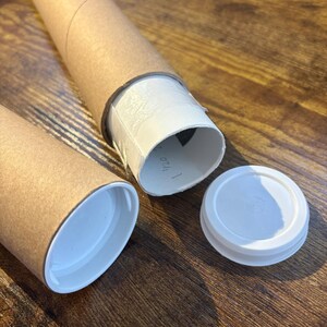 the print packaged for shipping. it is rolled into a tube and put inside a plastic sleeve. the plastic sleeved print is sticking out of a 2.5 inch mailing tube made of thick sturdy cardboard. another tube next to it is sealed with a plastic lid