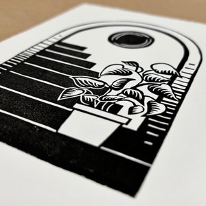 Angled close-up of the daytime archway print. The plant is in a large white pot on the bottom stair. The leaves of the plant have hatching shading lines. The sun  sits in the center of the sky under the arch and has thin white lines around its edges.