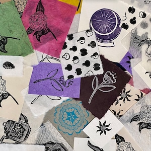 May include: A collection of handmade paper prints featuring various designs, including floral motifs, geometric patterns, and whimsical illustrations. The prints are in black and white, with some featuring pops of color like blue, purple, and red.