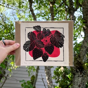 the print packaged on cardboard in a sealed plastic sleeve. the print is held in front of a lush tree