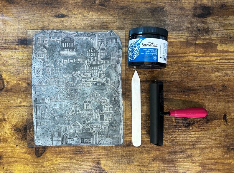 The linoleum block, ink, and rollers used to make this print. The block is a reverse image of the print. The block is glued onto a sheet of clear acrylic plastic for stability.