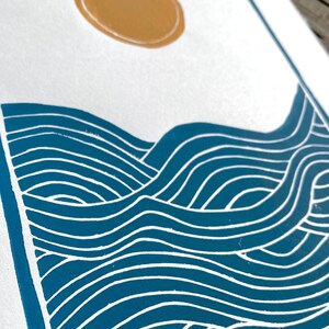 A closeup of the waves on the print, highlighting the blue ink and white lines between where the paper is showing through. the closeup shows a slight rough texture of the ink on the white paper.