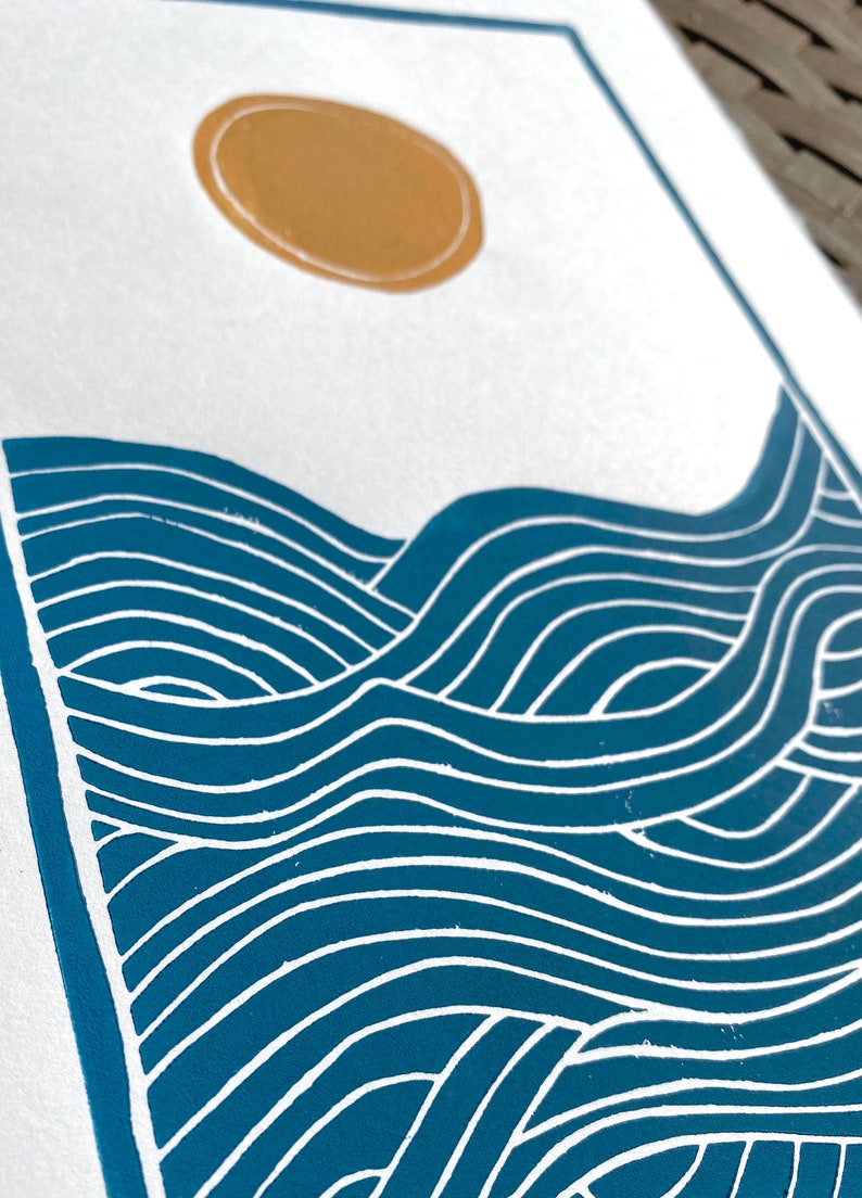 A closeup of the waves on the print, highlighting the blue ink and white lines between where the paper is showing through. the closeup shows a slight rough texture of the ink on the white paper.
