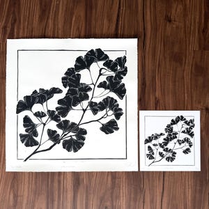 this print next to a reproduction print on a wooden background. the reproduction print has exactly the same image but is half as tall and half as wide as the original large print.