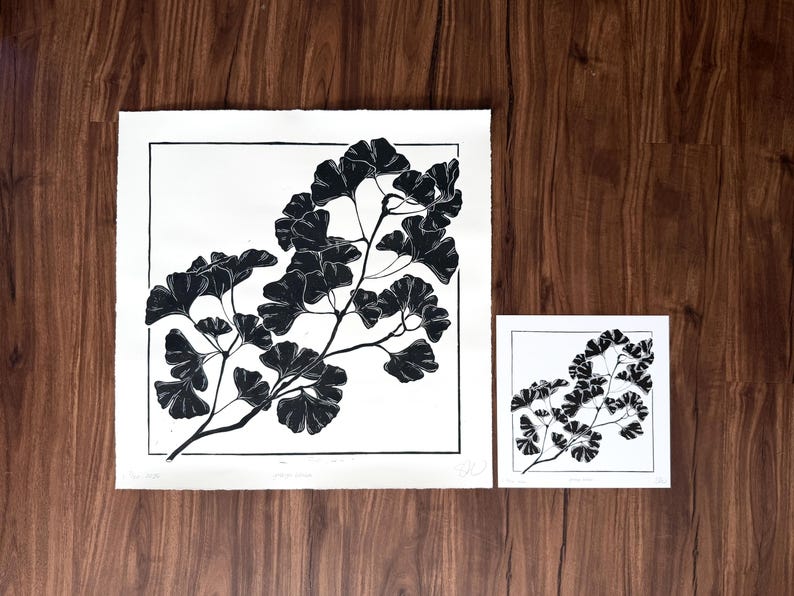 this print next to a reproduction print on a wooden background. the reproduction print has exactly the same image but is half as tall and half as wide as the original large print.