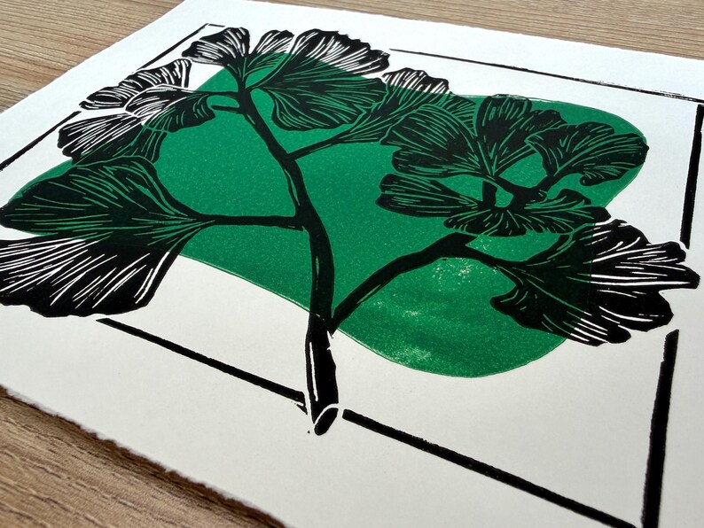 a closeup of the print from a low angle. the green blob behind the black ginkgo is visibly textured, giving the print a handmade feel.