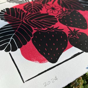 a close-up of the print, showing a few leaves and a strawberry. the leaves are black with white veins and the strawberries are black with white seeds. the red blob behind the black ink doesnt show through the black but adds dimension.