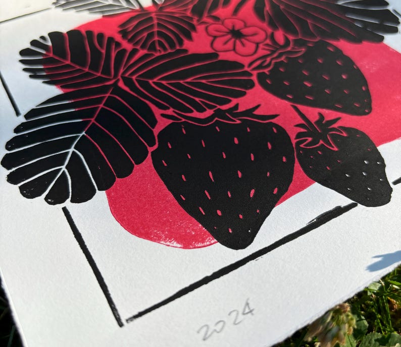 a close-up of the print, showing a few leaves and a strawberry. the leaves are black with white veins and the strawberries are black with white seeds. the red blob behind the black ink doesnt show through the black but adds dimension.