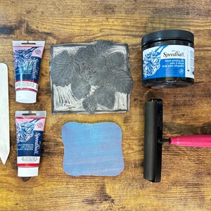 The linoleum block, ink, and rollers used to make this print. The block is a reverse image of the print.