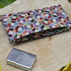 May include: A small, rectangular, fabric pouch with a colorful geometric pattern. The pouch is folded in half and sitting on a wooden surface. A silver lighter is also visible in the image.