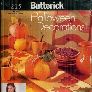 May include: Butterick Halloween Decorations pattern. The image features a variety of Halloween-themed decorations, including fabric pumpkins, mugs, a pie, and a decorative vase. The apron in the image has a pumpkin pattern.