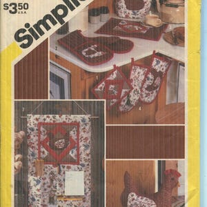 May include: A Simplicity 6144 sewing pattern envelope featuring illustrations of kitchen accessories including a chicken-shaped tea cozy, oven mitts, pot holders, a wall organizer with floral fabric, and a stuffed chicken figure on a yellow background.