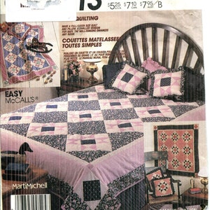 May include: A McCall's quilting pattern featuring a full/queen size quilt and pillow. The quilt has a patchwork design with pink, navy, and white squares. The pattern also includes a smaller version for baby and a wall hanging.
