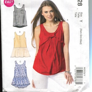 May include: McCall's M6928 sewing pattern featuring a woman in a red top. The pattern includes diagrams for tops with various designs, including a striped top and a floral print top. The pattern size is Y (Xsm-Sml-Med).