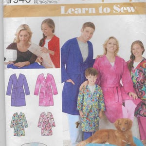 Könnte beinhalten: Simplicity Learn to Sew Schnittmuster mit einer Familie in Bademänteln. Das Schnittmuster enthält Anweisungen zum Herstellen von Bademänteln in verschiedenen Größen. Das Bild zeigt auch einen Hund auf einem blauen Kissen. Der Text auf dem Muster lautet "Learn Basic Skills".