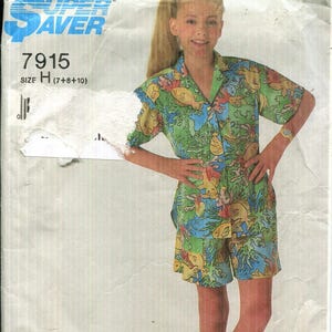 May include: Simplicity Patterns sewing pattern envelope featuring a young person wearing a matching short-sleeved shirt and shorts set. The outfit has a colorful fish and coral print. The envelope has the number 7915 and size H.