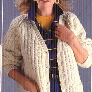 May include: A white knitted cardigan with a cable knit pattern and button closure. The cardigan has two pockets and a 1192-554 label.