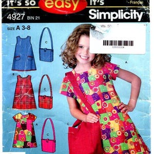 Pode incluir: Um envelope de molde de costura Simplicity 4927 para um vestido de manga curta e uma bolsa de ombro. A embalagem exibe ilustrações das peças em vários padrões de tecido e cores, incluindo designs florais, xadrez e lisos em vermelho ou amarelo.