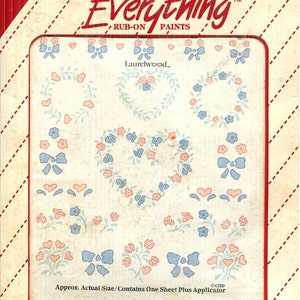 Puede incluir: Una hoja de pintura para frotar Plaid Accents On Everything con varios diseños florales y de lazos en azul claro y rosa. El empaque incluye el texto Accents On Everything, Laurelwood e instrucciones de uso sobre un fondo crema.