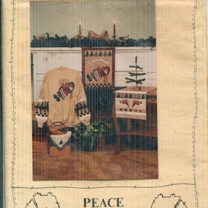 May include: A Homespun Christmas pattern featuring a beige sweatshirt with a Christmas design, a framed wall hanging, and a small table with a runner. The image has a rustic, country aesthetic, with the text "Peace Creek Collections" and "no. 24".