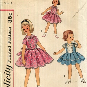 Puede incluir: Sobre de patrón Simplicity vintage con ilustraciones de tres vestidos infantiles. Los vestidos son rosas y azules, con estampados florales y ribetes de encaje. El sobre dice "2436 Child Size 2" y "Simplicity Printed Pattern 35c".