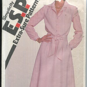 May include: A vintage Simplicity ESP Extra-Sure Pattern envelope featuring a pink dress design. The dress has long sleeves, a collared neckline, and a tie belt. The envelope displays the number 5279 and the price $1.25.