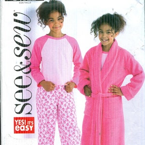 May include: A See & Sew B4322 sewing pattern envelope featuring illustrations of two outfits: a long-sleeve shirt with pink sleeves and white bodice paired with pink patterned pants, and a solid pink robe worn over matching pink patterned pants.